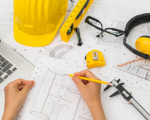 Hand over Construction plans with yellow helmet and drawing tools on blueprints