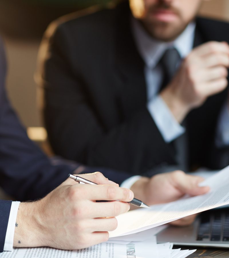 Closeup portrait of two unrecognizable  business partners reviewing paperwork and signing contract papers at table during meeting